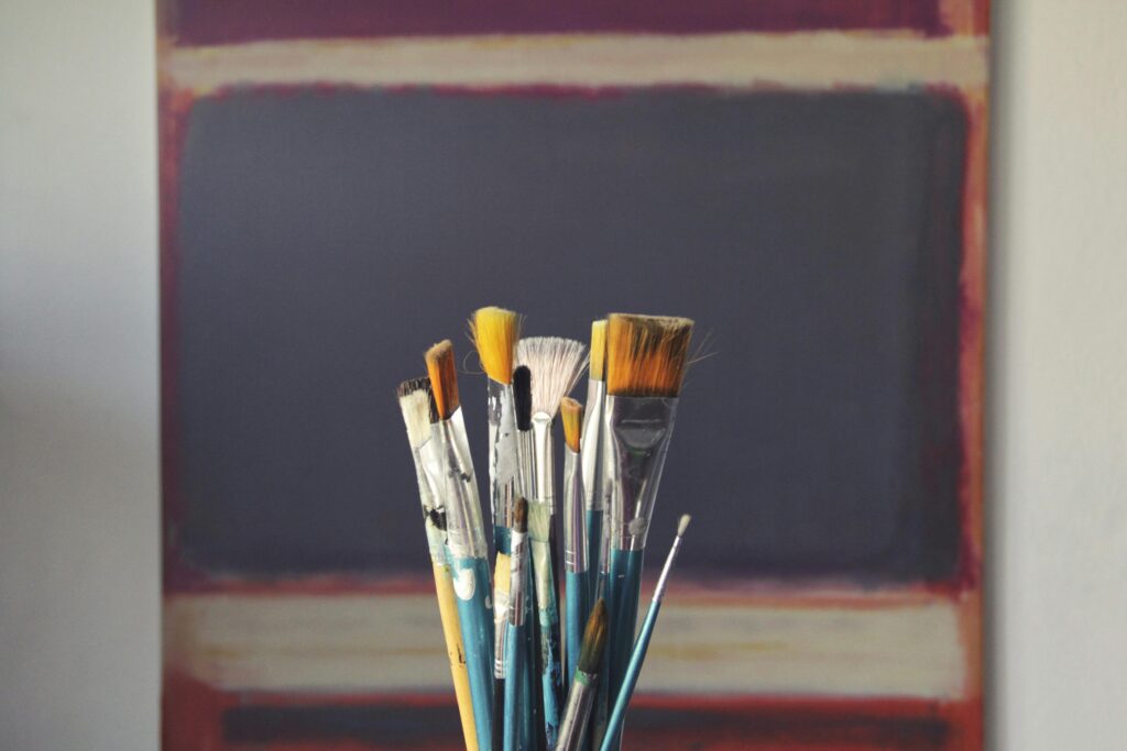 A set of paintbrushes in front of an abstract canvas, reflecting creativity and inspiration.